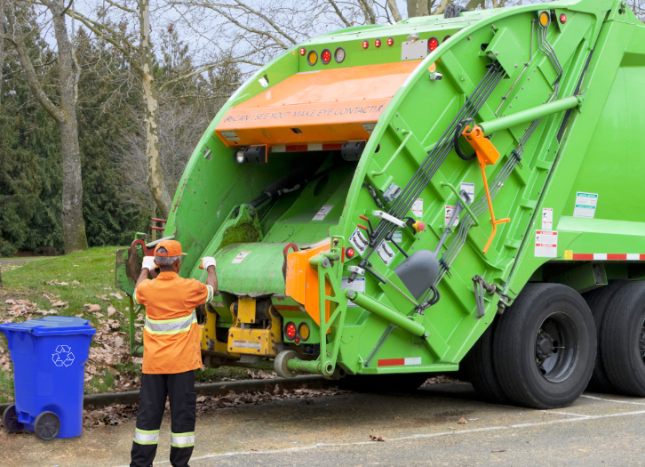 Garbage worker signals truck to back up for collection of blue curbside recycling bin