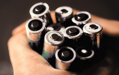 Hands holding onto a lot of single use AA batteries