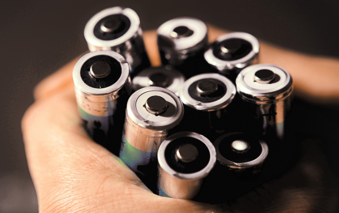 Hands holding onto a lot of single use AA batteries